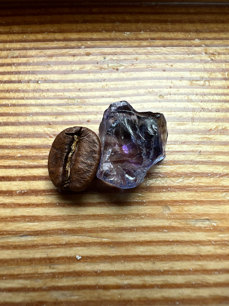 Natural Tanzanite Rough showing blue and purple Beside Coffee Bean- Rough stone is larger